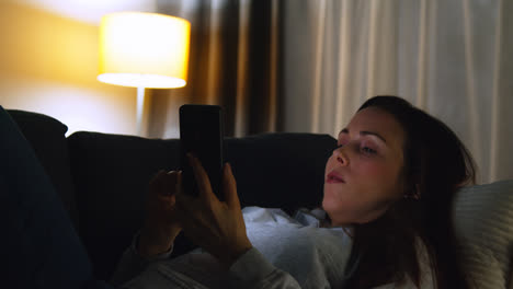 Woman-Lying-On-Sofa-At-Home-At-Night-Streaming-Or-Looking-At-Online-Content-On-Mobile-Phone-8